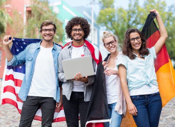 Group of happy friends holding national flag and using laptop